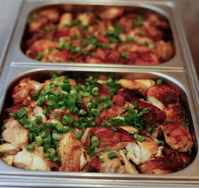 Hot grilled chicken with green onions in stainless catering trays for a party buffet.